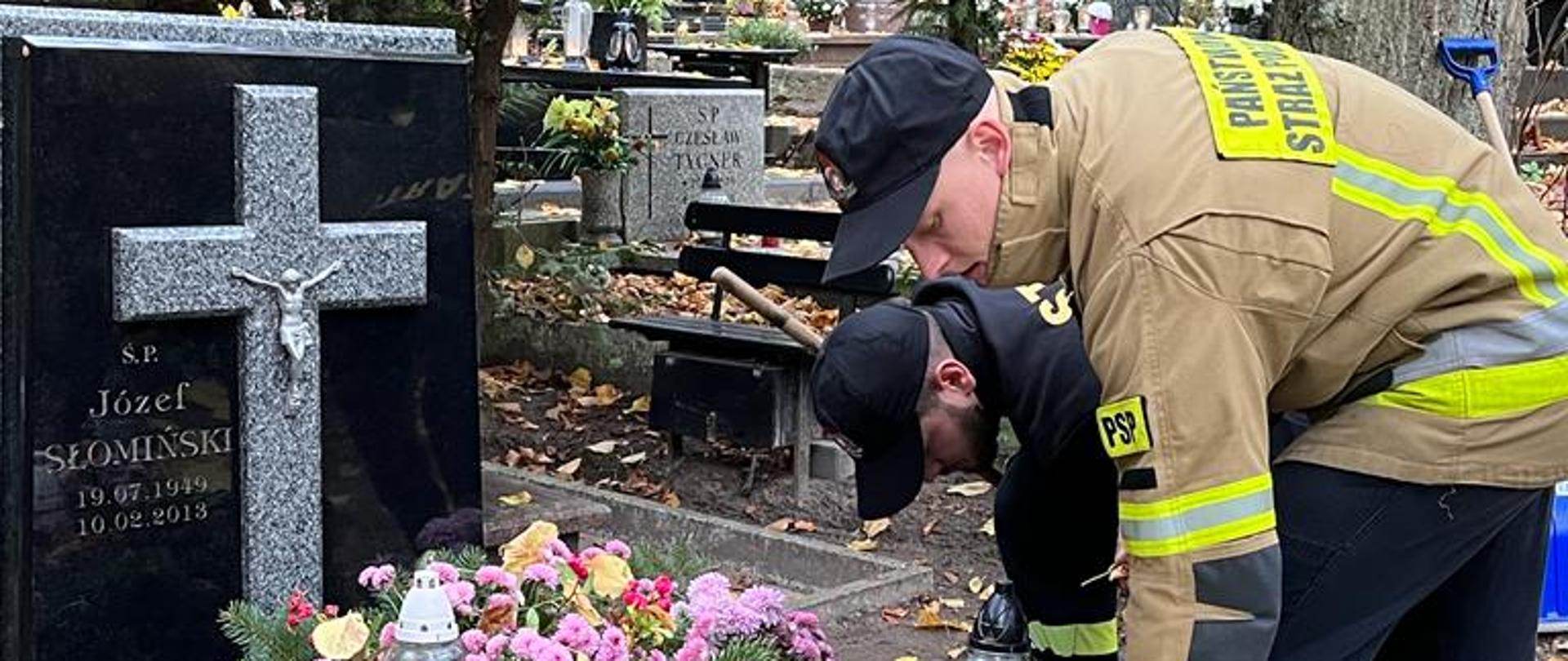 Strażacy pochyleni nad grobem, czyszczą go i odpalaja znicz