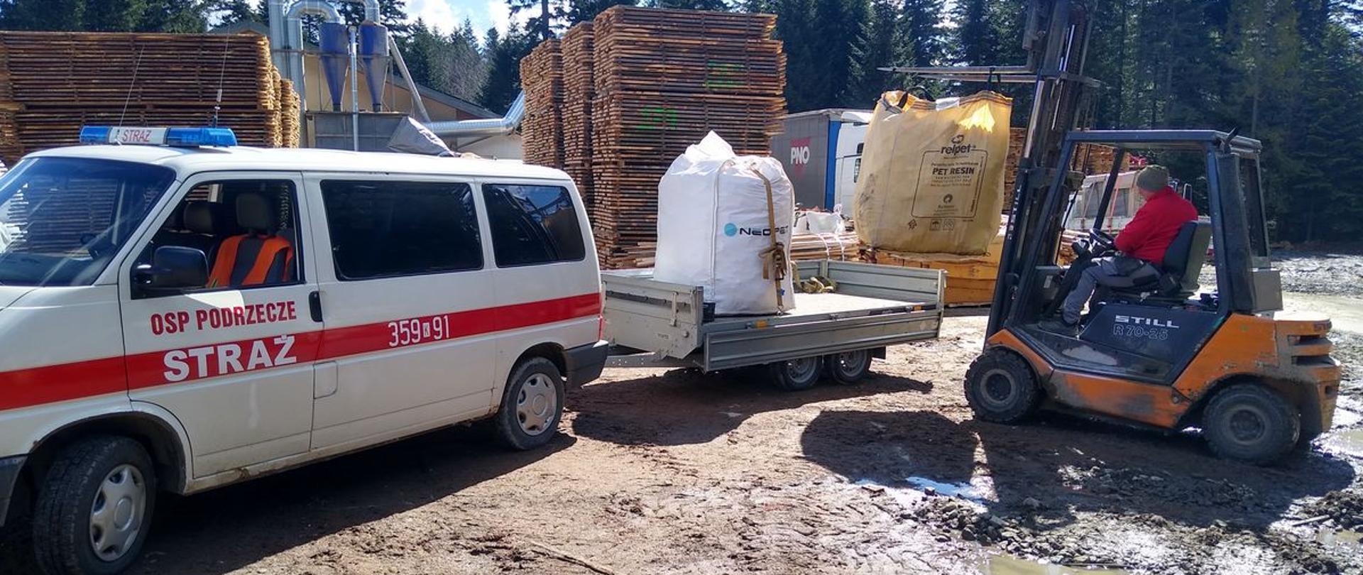 Samochód strażacki z przyczepka na który jest ładowany opał wózkiem widłowym.