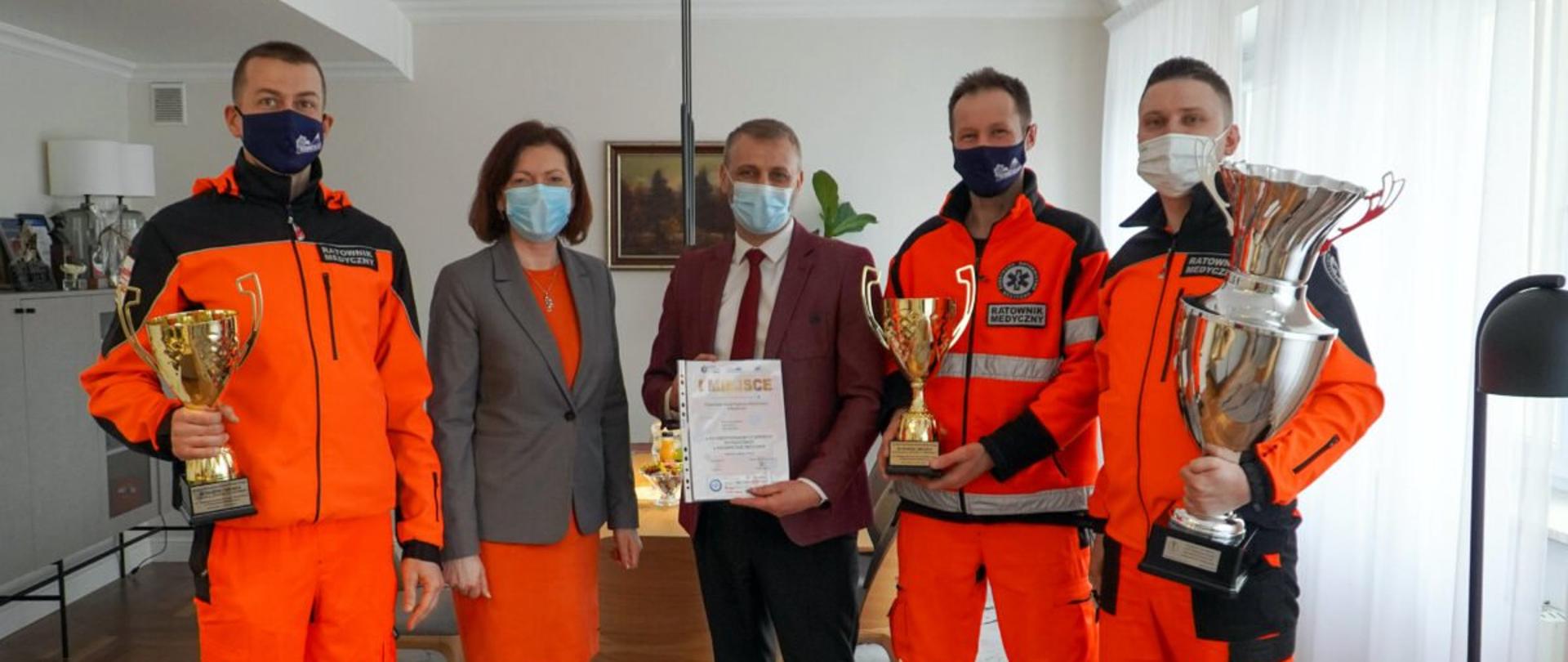 Wojewoda podkarpacki Ewa Leniart w otoczeniu ratowników z Wojewódzkiej Stacji Ratunkowej w Rzeszowie oraz dyrektora Stacji Andrzeja Kwiatkowskiego. Trzech ratowników znajdujących się we wnętrzu gabinetu wojewody trzyma puchary. 