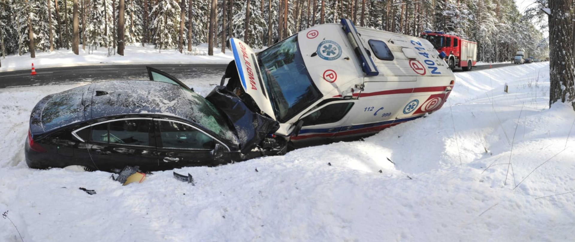 Ambulans i samochód osobowy leżące na boku w rowie po zderzeniu czołowym.