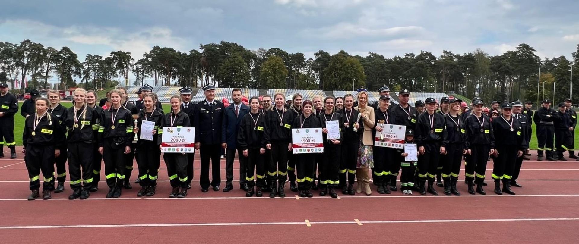 drużyny z medalami i pucharami na boisku podczas Powiatowych Zawodów Sportowo- Pożarniczych powiatu kozienickiego.