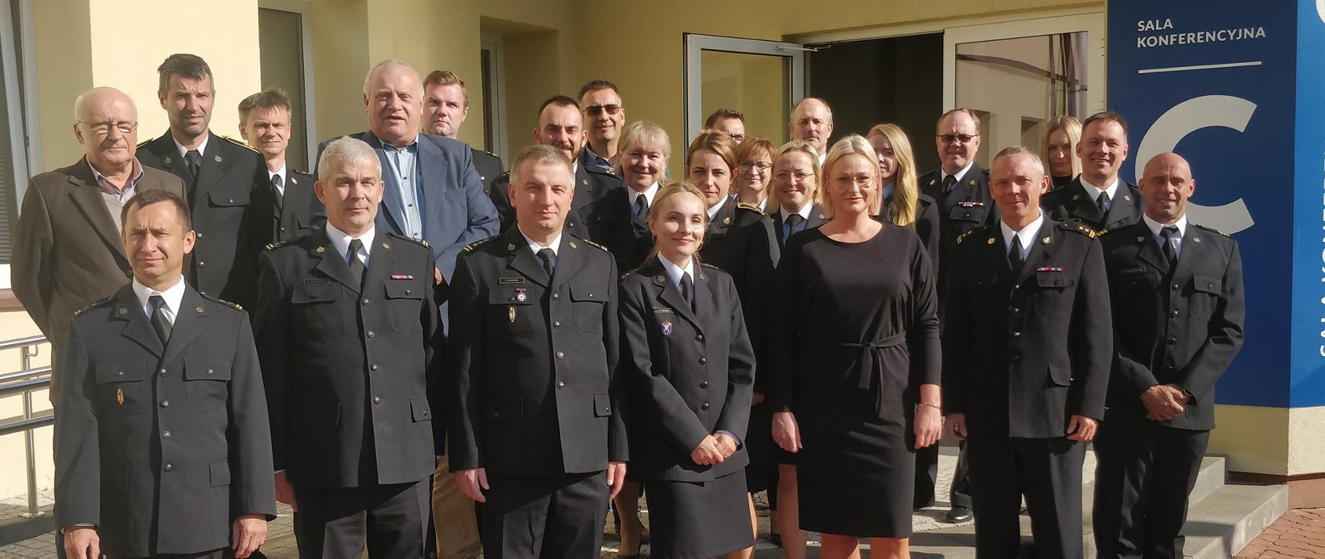 Grupa osób tj. funkcjonariusze PSP oraz osoby cywilne - członkowie narady pozują przed budynkiem do zdjęcia grupowego