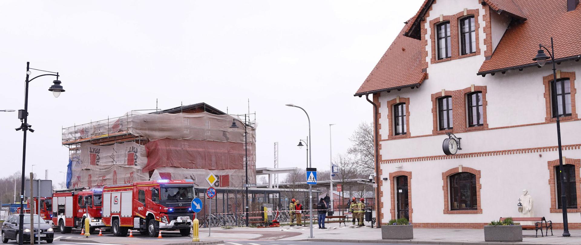 Zdjęcie z oddali obejmujące budynek dworca, wydzielony teren ćwiczeń ze strażakami oraz wozami strażackimi