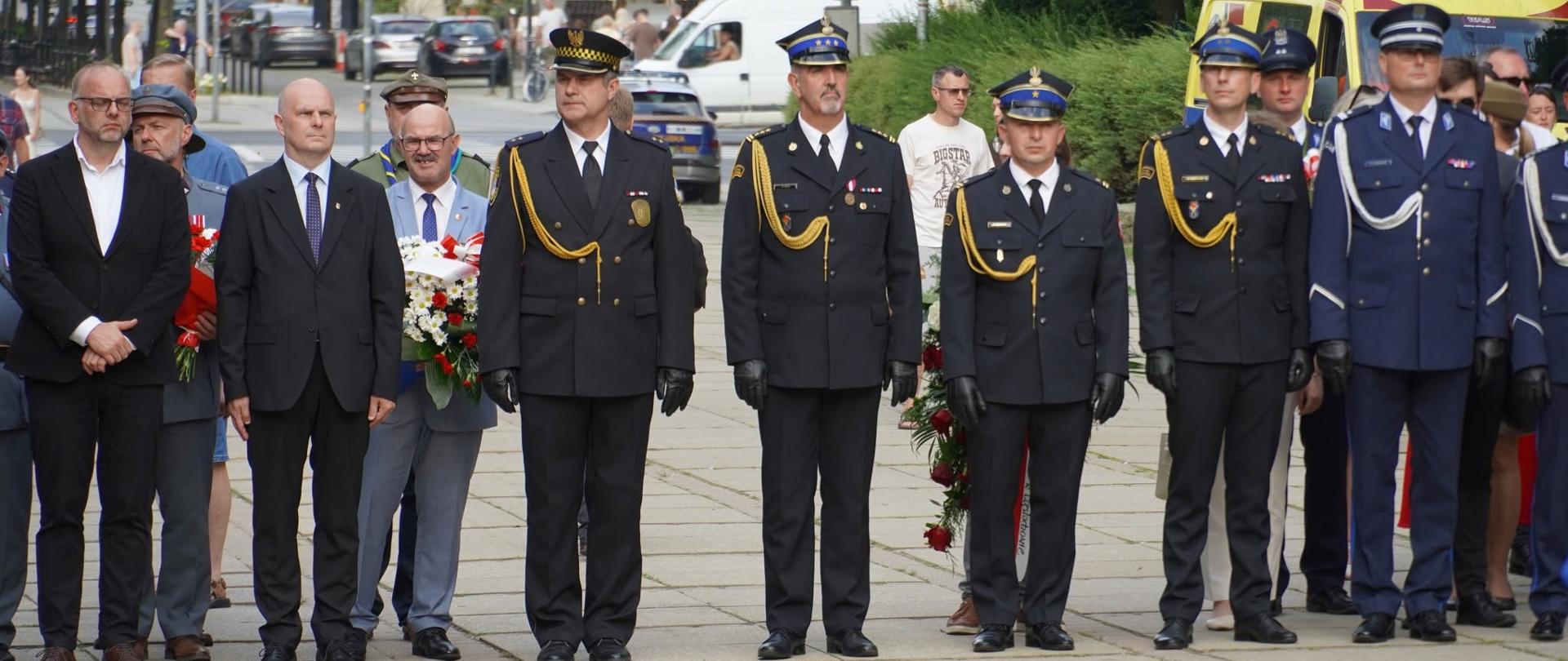 Przedstawiciele władz państwowych oraz funkcjonariusze służb mundurowych stojący w rzędzie podczas uroczystości