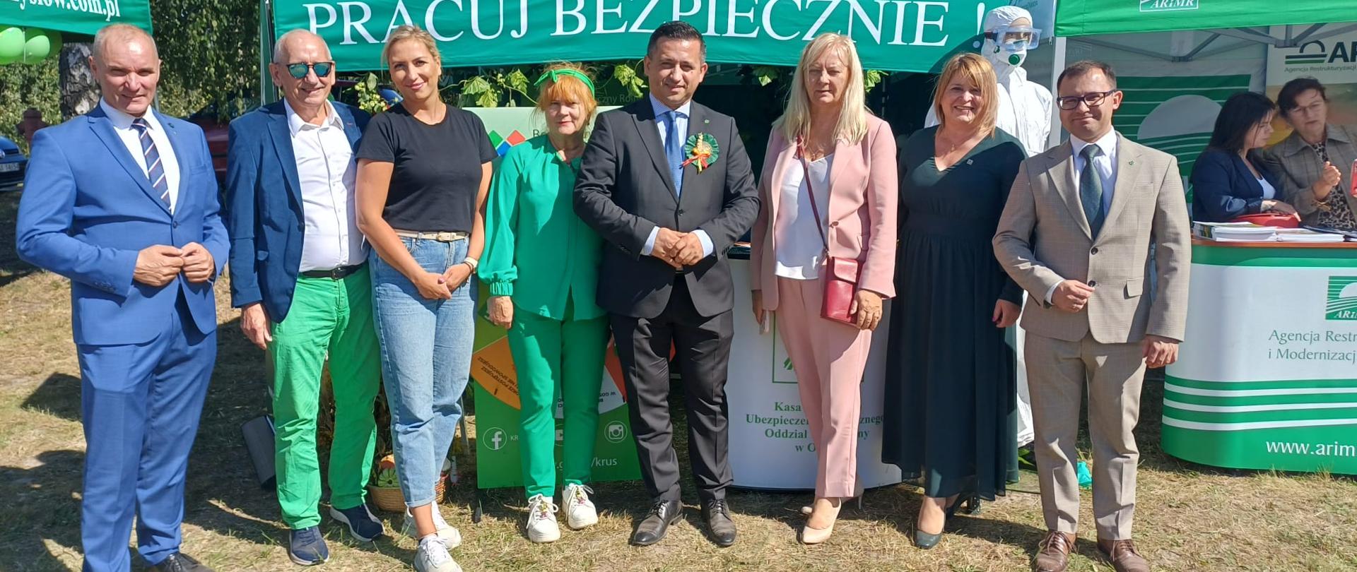 Cztery kobiety i czterech mężczyzn przy zielonym namiocie ze stoiskiem KRUS z napisem: Pracuj bezpiecznie!