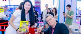 一位喜爱科幻文学的女读者手里拿着小说《赛博朋克2077：无人幸存》，与作者波兰科幻大师拉法乌·科西克一起合影。波兰作者正在参加签名活动。