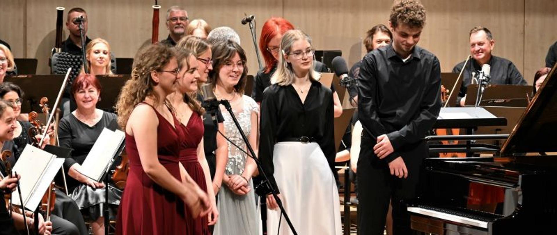 Zdjęcie przedstawiające solistów koncertu na scenie słupskiej filharmonii. W tle orkiestra.