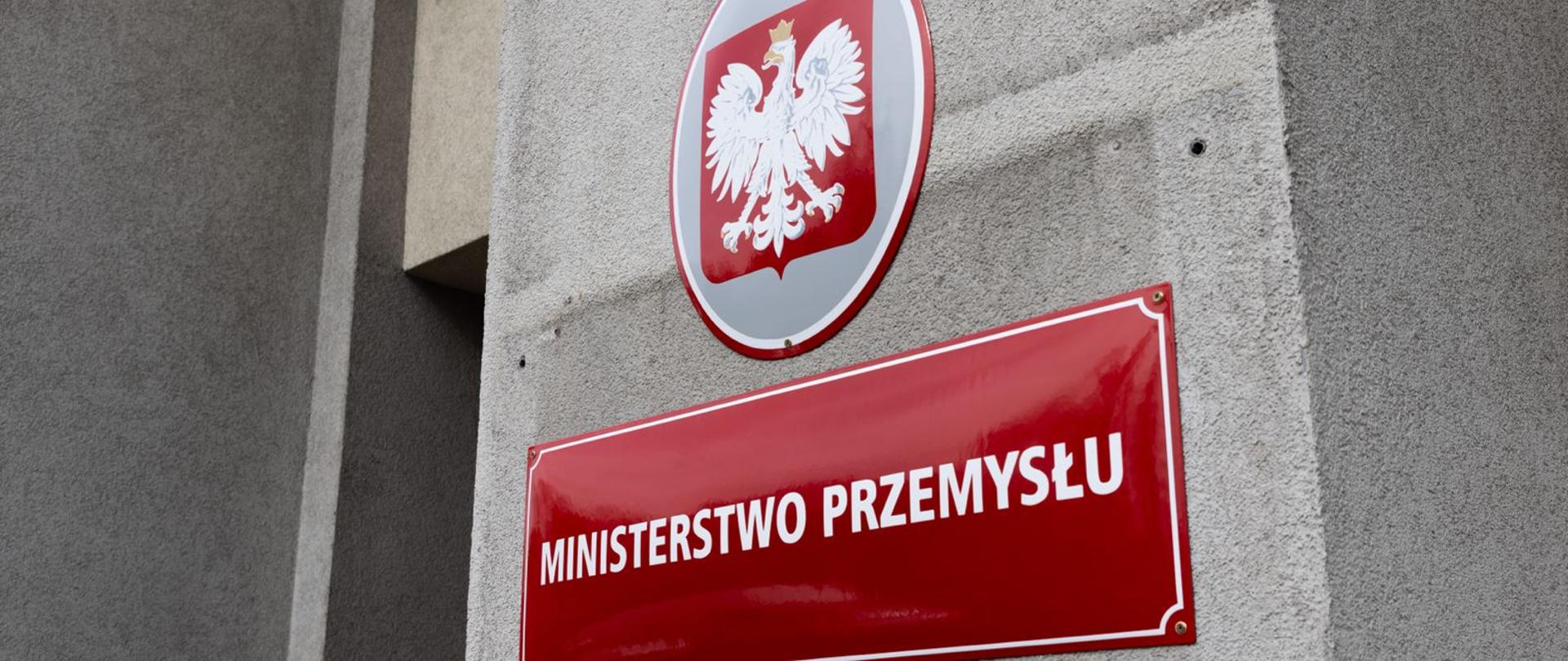 Owalne godło i tabliczka z białym napisem "Ministerstwo Przemysłu" umieszczone na budynku.