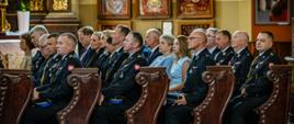 Zdjęcie przedstawia gości zaproszonych na uroczystości. Goście siedzą w ławkach w kościele podczas mszy. 