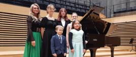 Pani Iwona Ulbrich z czterema uczennicami i uczniem przy fortepianie na scenie sali koncertowej PSM