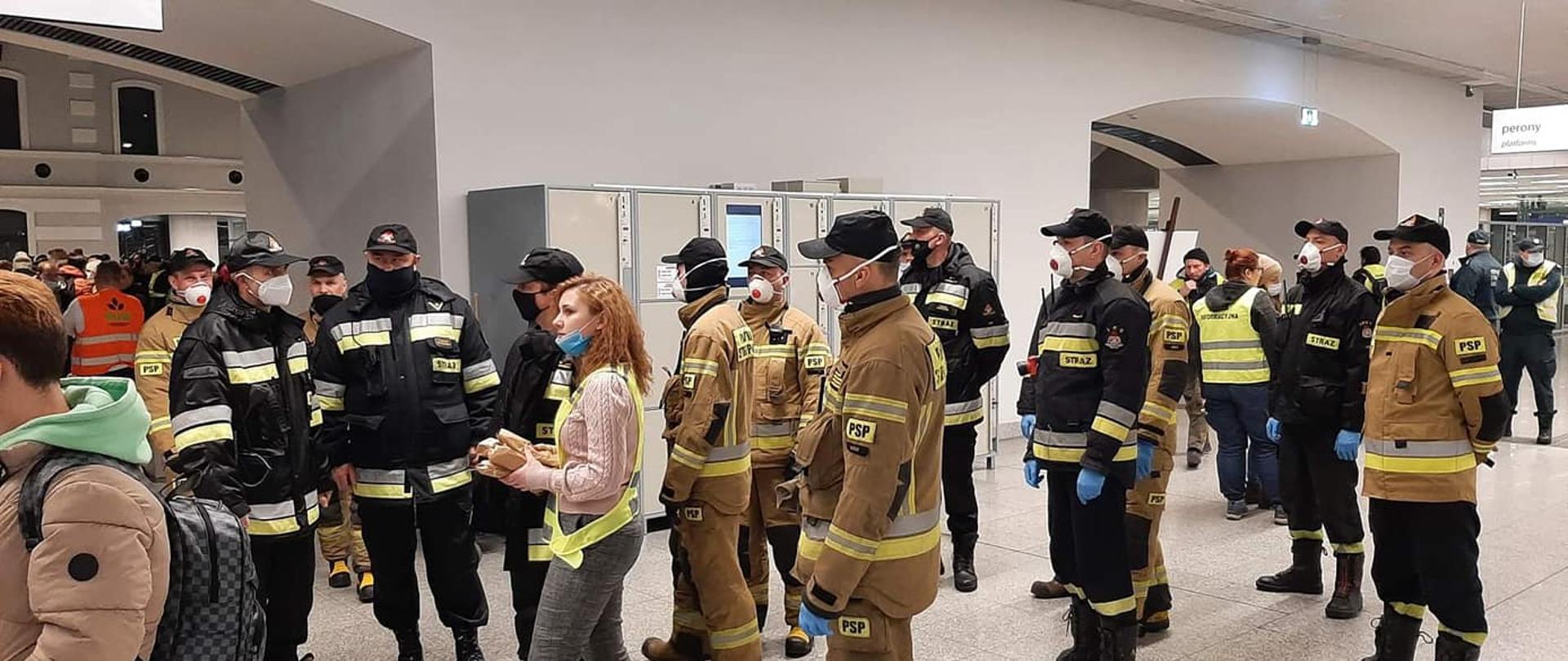 Grupa strażaków stojących na dworcu kolejowym.