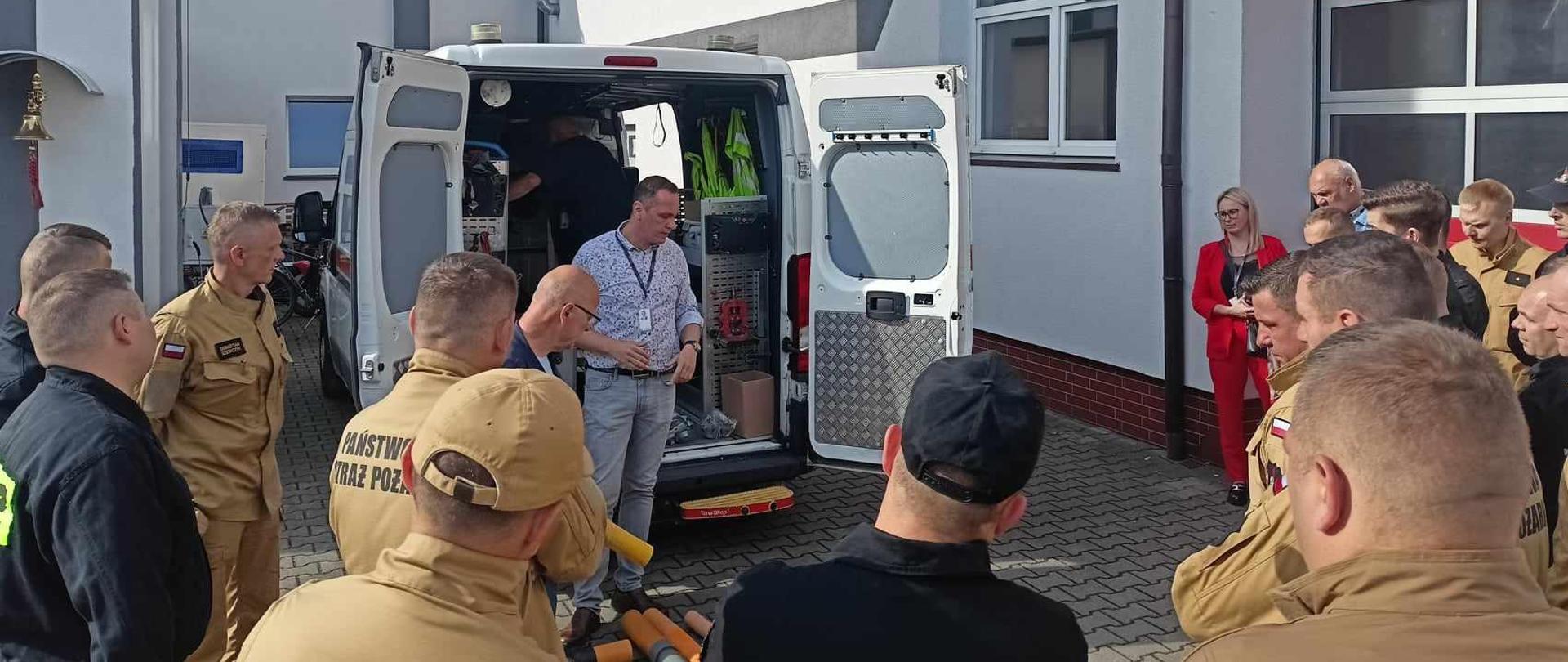 Zdjęcie przedstawia strażaków w umundurowaniu służbowym oraz pracowników Polskiej Spółki Gazowniczej podczas szkolenia przy samochodzie Pogotowia Gazowego na placu Komendy. 