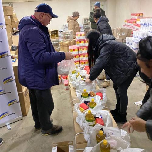 W magazynie grupa osób pakuje produkty żywnościowe do plastikowych siatek