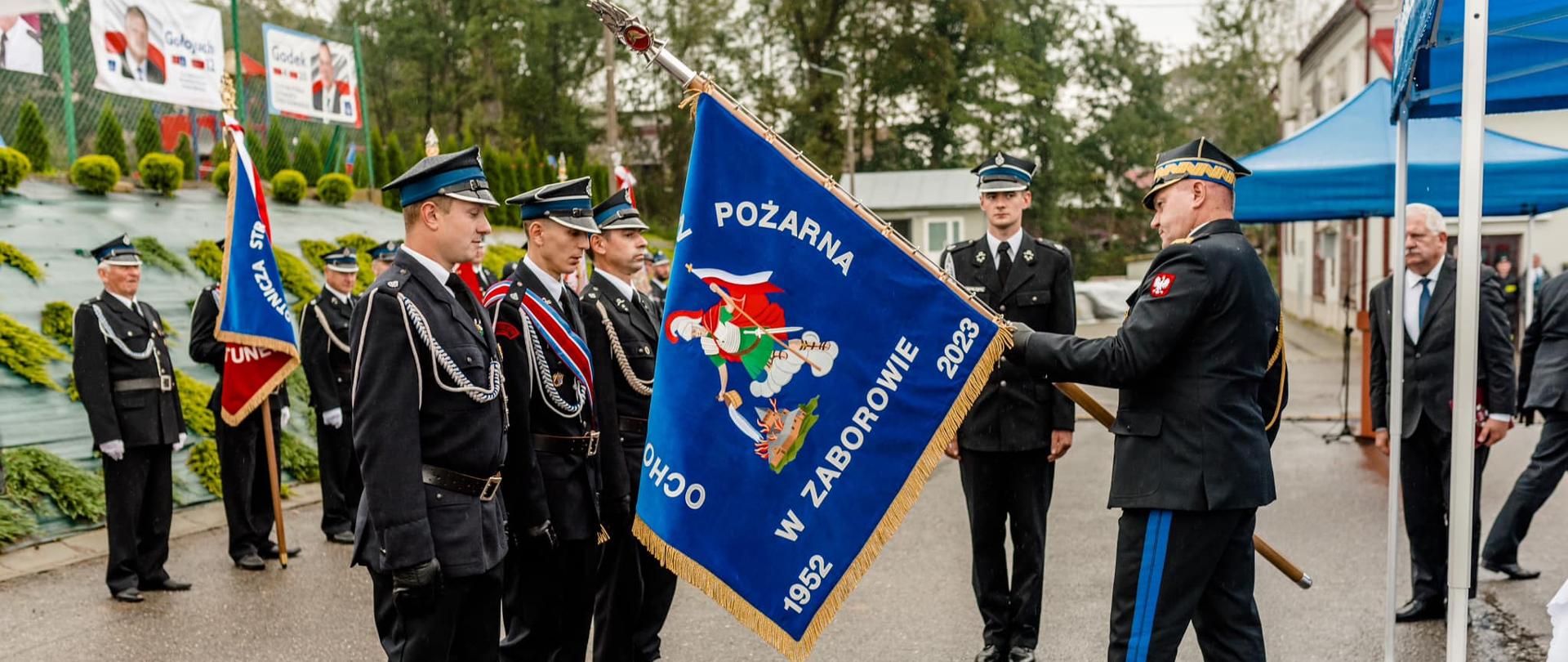 Na zdjęciu został uchwycony moment przekazywania sztandaru przez Komendanta Wojewódzkiego PSP w Rzeszowie w ręce pocztu sztandarowego OSP Zaborów. W tle druhowie OSP stoją w szeregu.