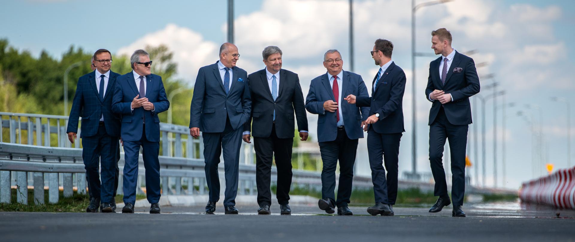 ośmiu mężczyzn, w tym wicewojewoda łódzki Marcin Buchali, minister Zbigniew Rau, minister Waldemar Buda, marszałek Grzegorz Schreiber idą nowo otwartym odcinkiem drogi s14