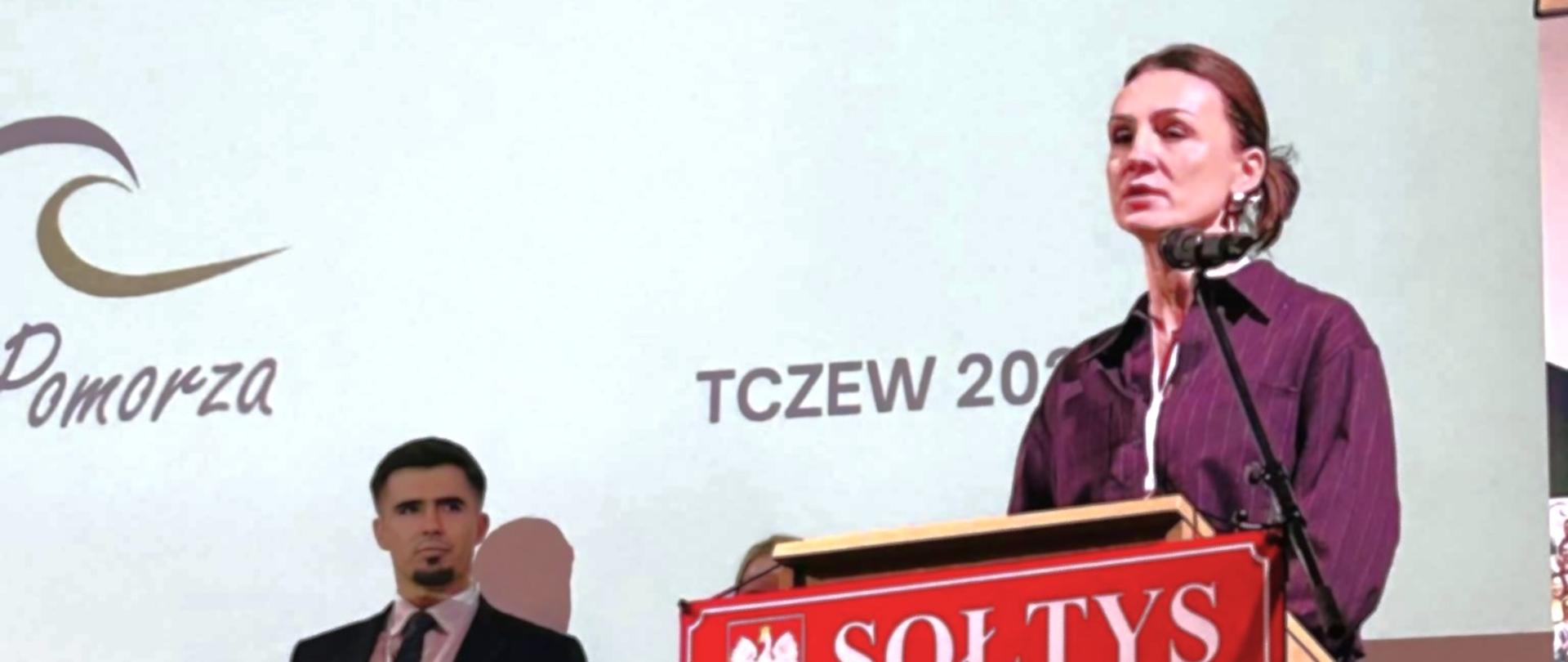 Kobieta (wojewoda) stoi za pulpitem z napisem sołtys i przemawia