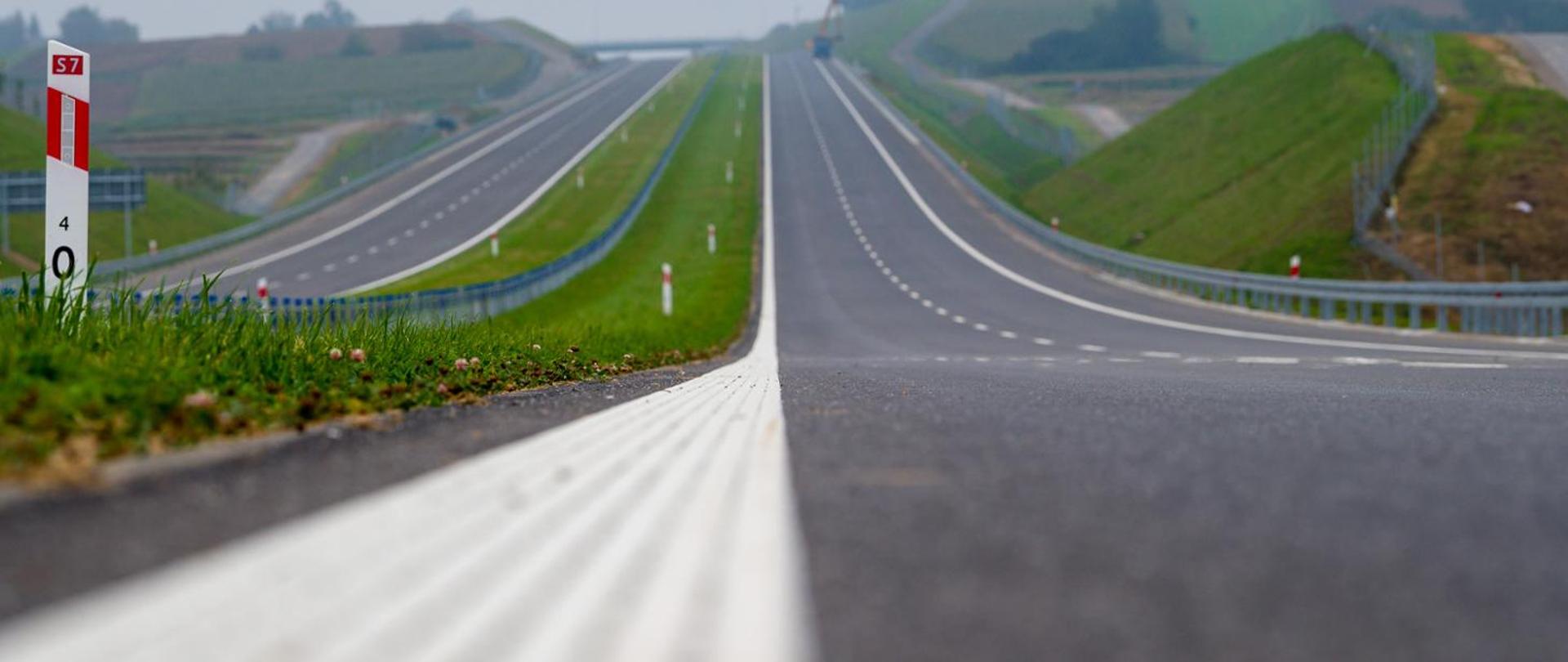 Widok z poziomu ziemi na jezdnię drogi ekspresowej. Widoczny pas rozdziału i pikietaż