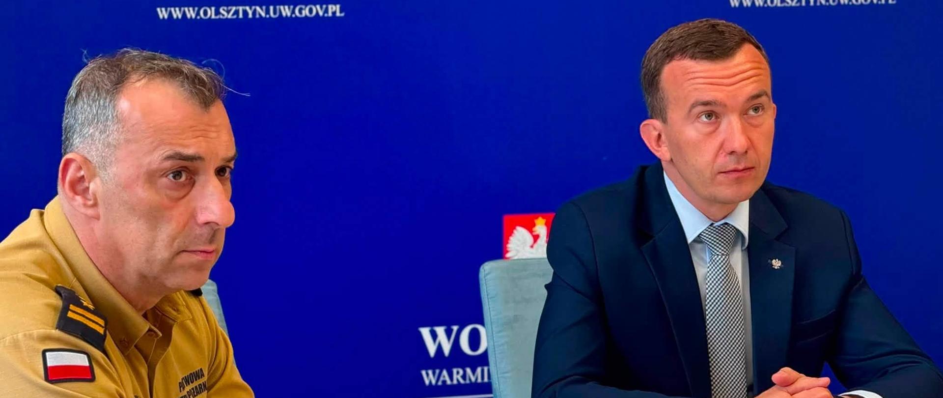 Mężczyzna w garniturze, wicewojewoda, oraz mężczyzna w mundurze straży siedzą przy konferencyjnym stole i patrzą w stronę monitora 