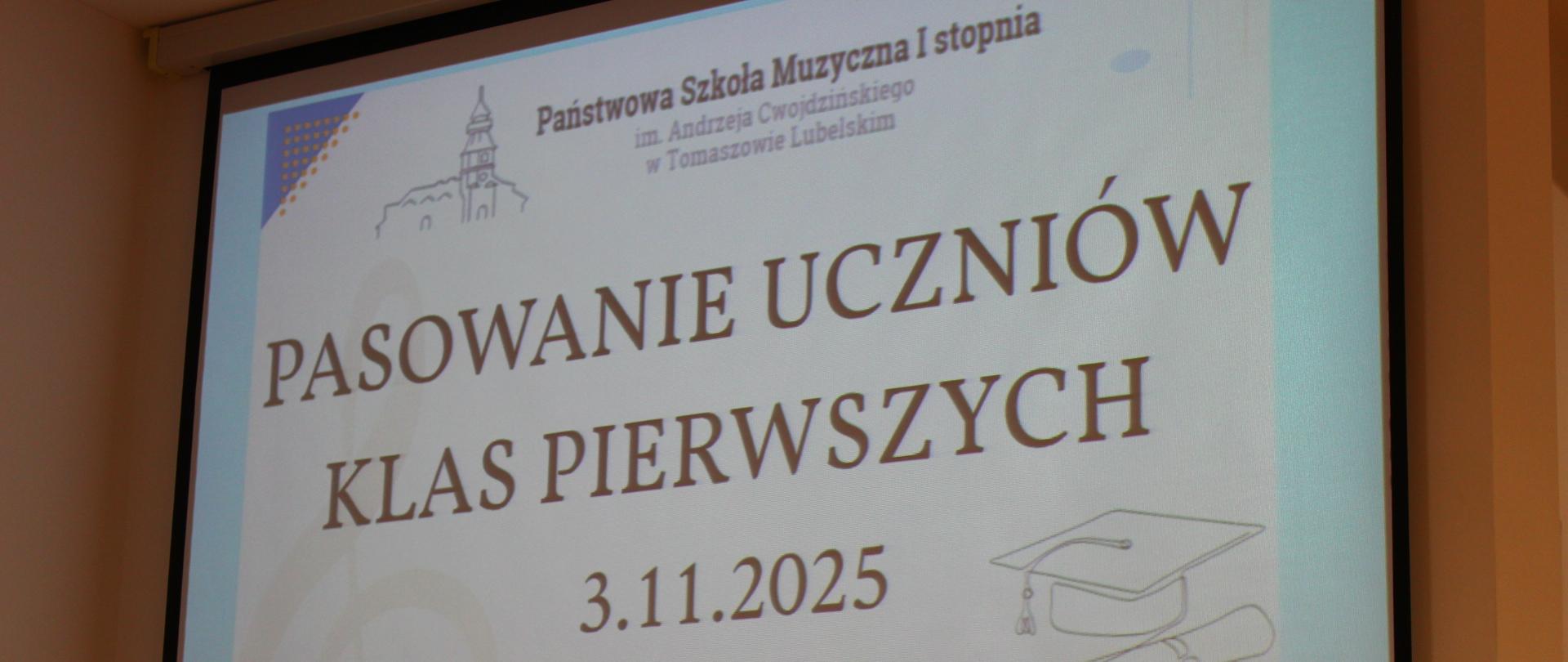 projektor z wyświetlanym plakatem na uroczyste pasowanie uczniów klas pierwszych, zawiera klucz wiolinowy, pięciolinię z nutami, kolorowe kółka, prostokąty, symboliczny biret z dyplomem, logo szkoły oraz tytuł wydarzenia