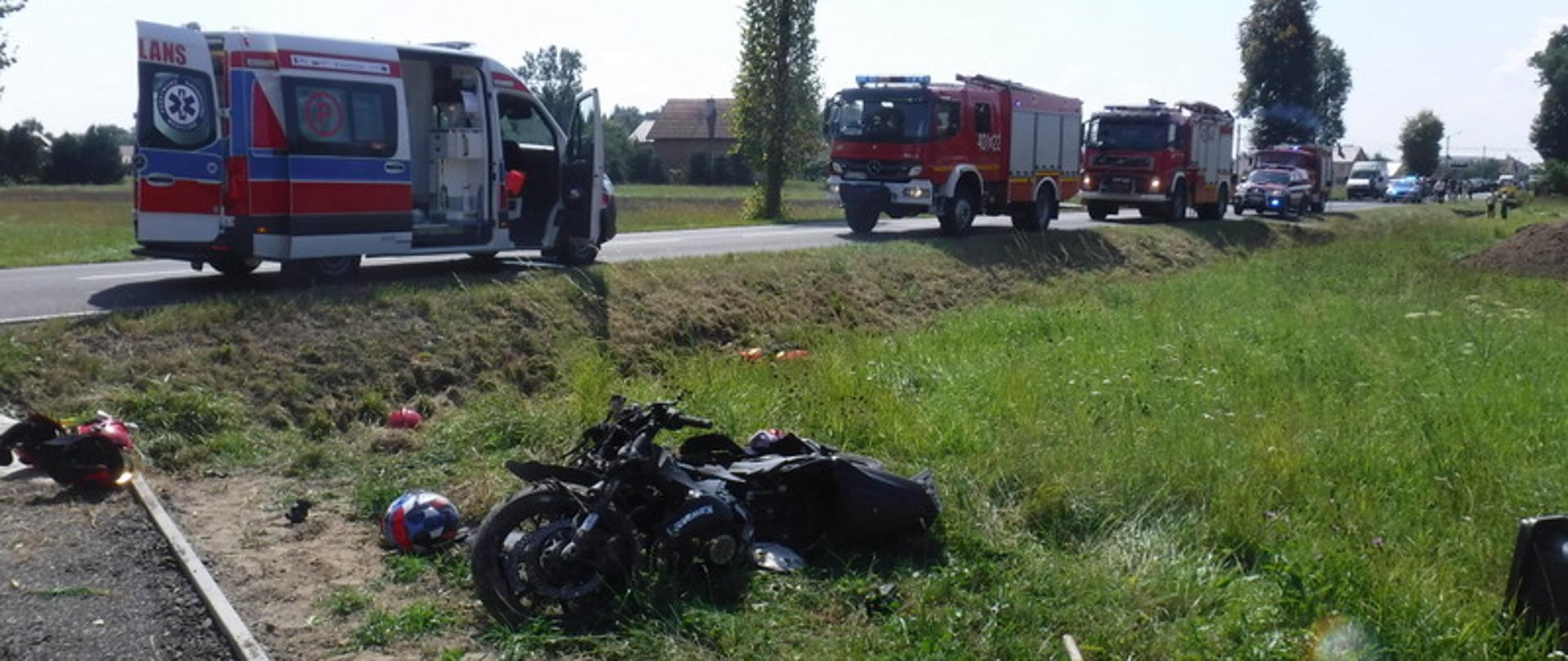 Zdjęcie główne przedstawia rozbity motocykl znajdujący się w przydrożnym rowie. Na drodze stoi ambulans ZRM oraz samochody pożarnicze z JRG Bochnia: GBARt 2,5/16, SCRt, SLRR.