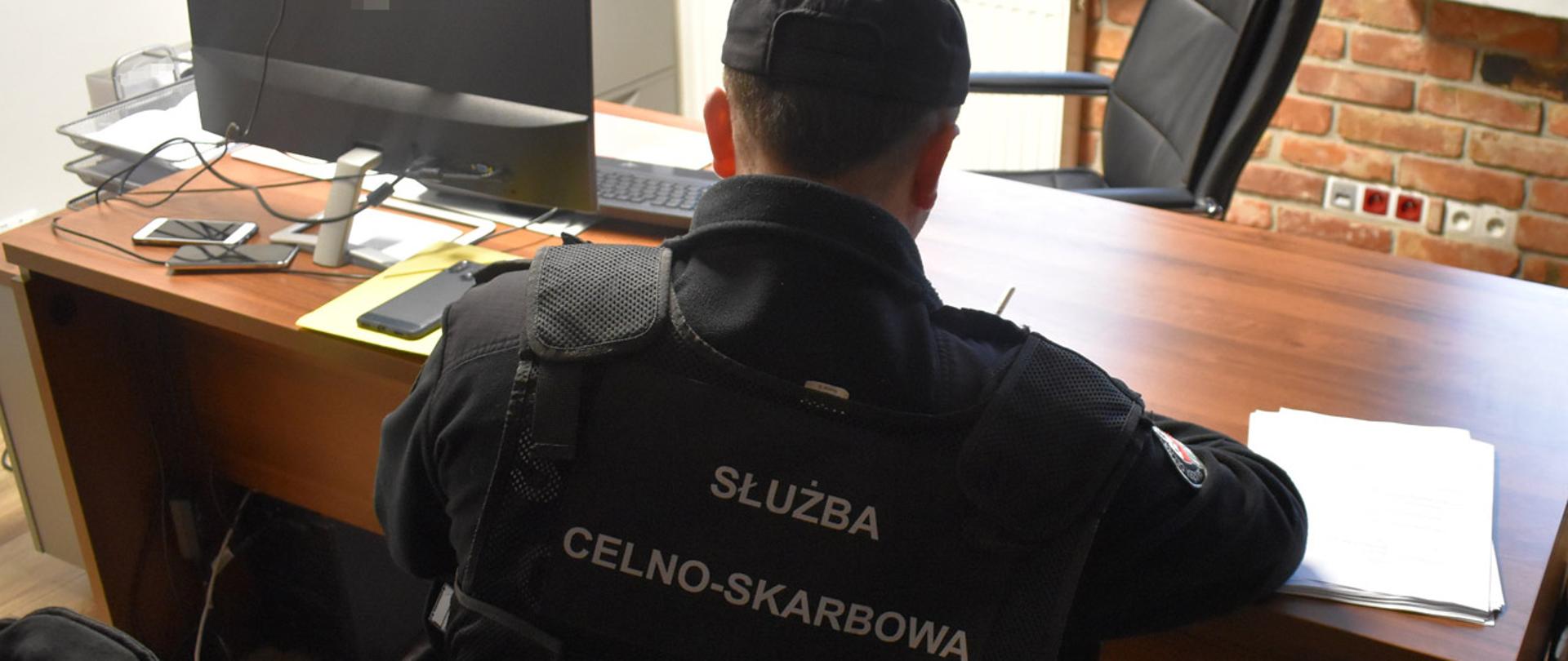 Funkcjonariusz Służby Celno-Skarbowej przy biurku podczas przeglądania dokumentów.