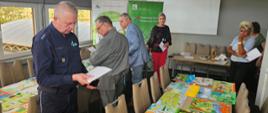 W pokoju konferencyjnym trzy kobiety i trzech mężczyzn, jeden z nich mundurze policyjnym, stoi z notatkami w rękach przy dwóch stołach, na których leży kilkadziesiąt prac plastycznych dzieci. 