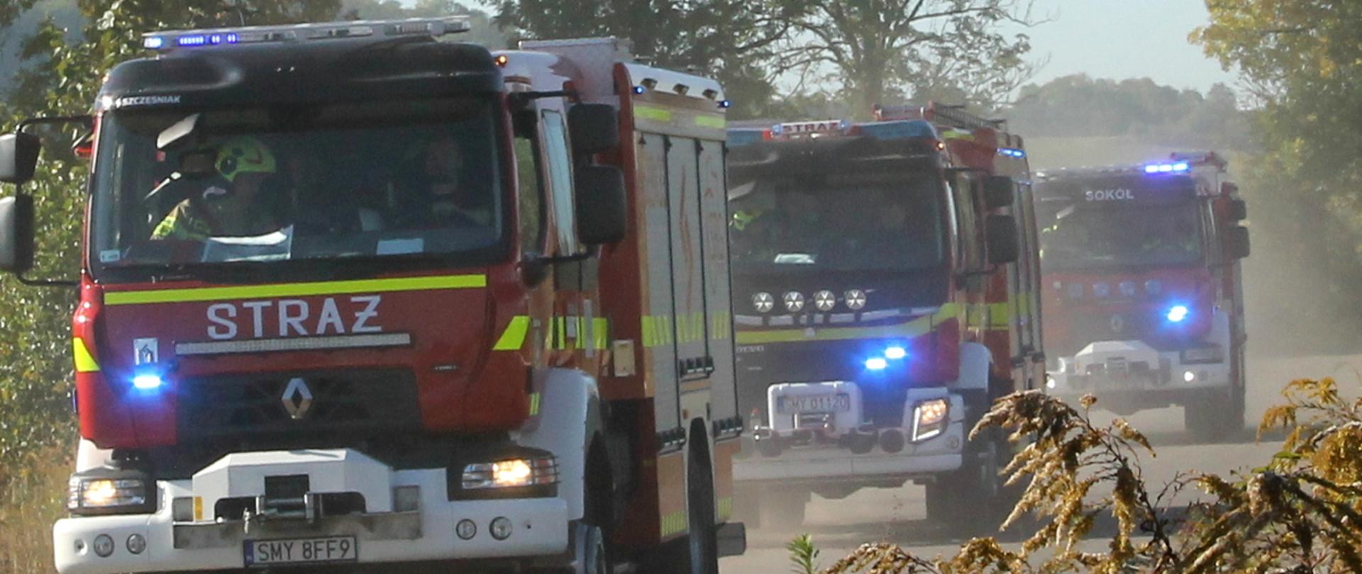 Zdjęcie przedstawia pojazdy pożarnicze z włączonymi sygnałami świetlnymi podczas realizacji zadań ratowniczo-gaśniczych w trakcie ćwiczeń Kompanii Gaśniczej OSP nr 8 „Myszków” pk. „ZAKŁAD 2026