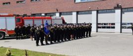 Na zdjęciu widoczni strażacy w umundurowaniu galowym ustawieni w trzech rządach. Czwarty rząd to strażacy w umundurowaniu koszarowym. W tle widoczne wozy gaśnicze.