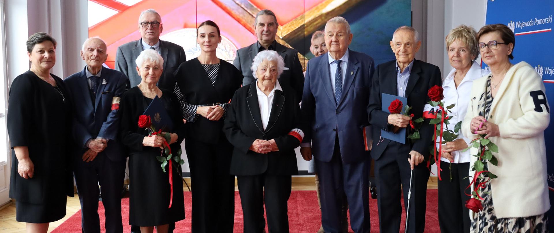 grupa osób stoi w sali, w tle na telebimie zdjęcie medalu Sint Sua Praemia Laudi