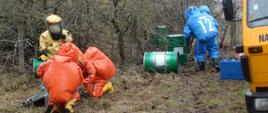 Pięciu strażaków w ubraniach chemicznych podczas dokonywania pomiaru wycieku substancji z metalowych beczek
