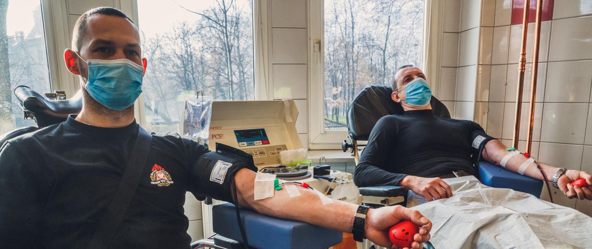 Na zdjęciu widoczna jest sala zabiegowa w stacji krwiodawstwa. W sali dwóch strażaków siedzi na fotelach zabiegowych, strażacy są podpięci do urządzeń, które pobierają osocze.