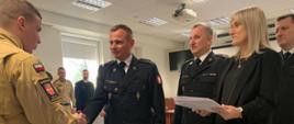 Zastępca Komendanta Centralnej Szkoły PSP gratuluje funkcjonariuszowi PSP ukończenia szkolenia, obok stojący Mazowiecki Komendant Wojewódzki PSP oraz kobieta trzymająca białe teczki