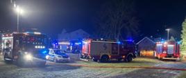 zdjęcie wykonane w nocy cztery wozy strażacki i jeden samochód policyjny stoją na łące przed budynkami 