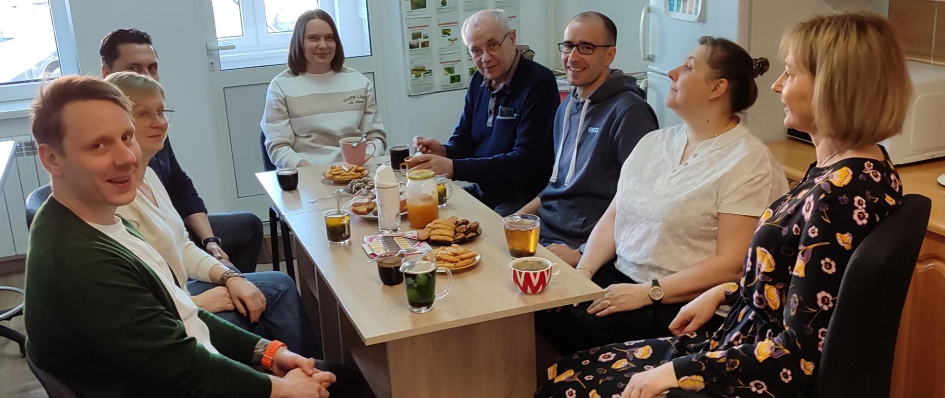 Grupa osób uczestniczących w spotkaniu siedzących przy stole.