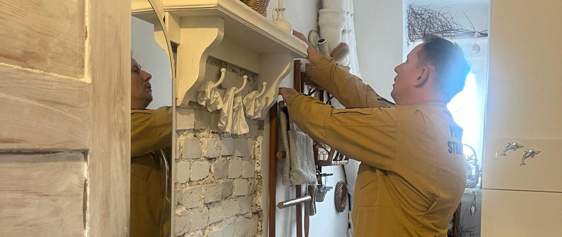 Strażak ubrany w mundur koloru piaskowego montuje czujkę tlenku węgla w przedpokoju.