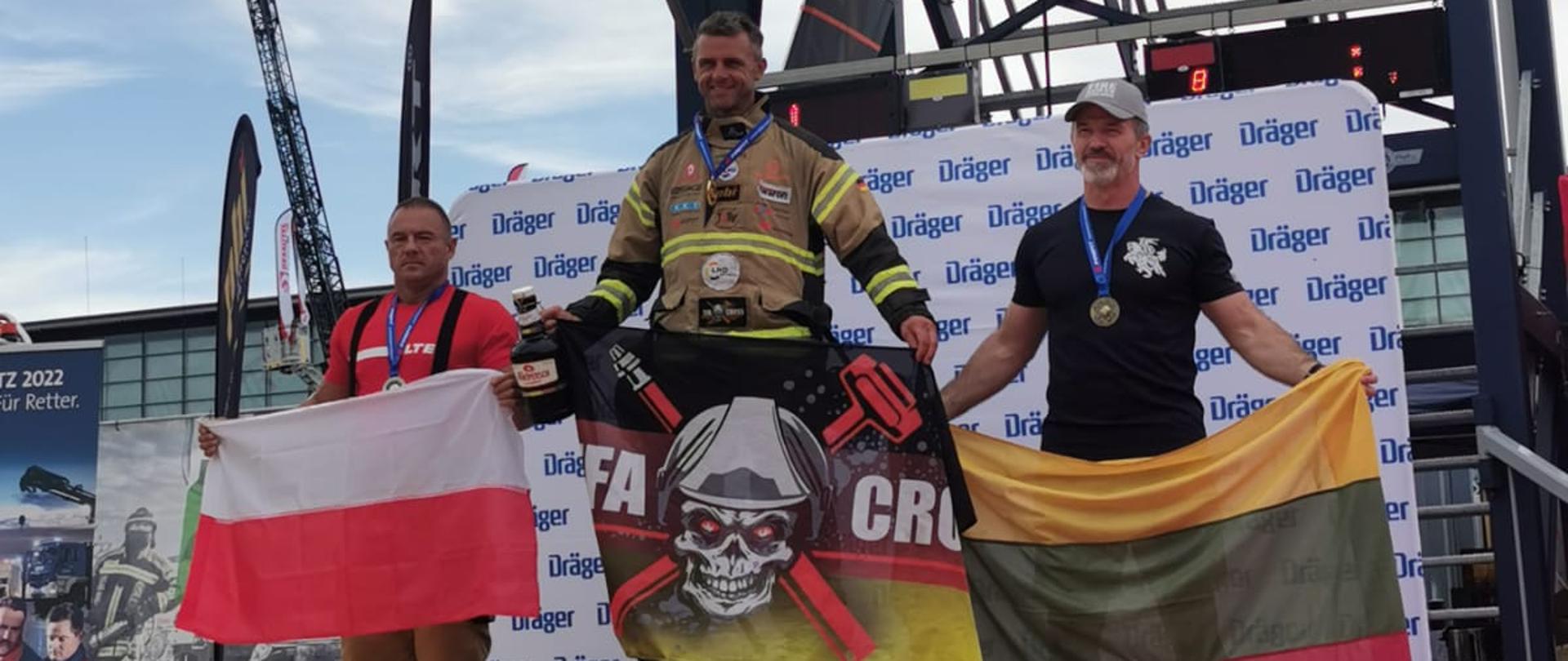 Zdjęcie przedstawia zawodników stojących na podium podczas zwodów Mistrzostwa Europy w formule Firefit w Hanowerze. Stoją z wywieszonymi flagami, na pierwszym miejscu Niemcy, na drugim Polska, na trzecim Litwa.