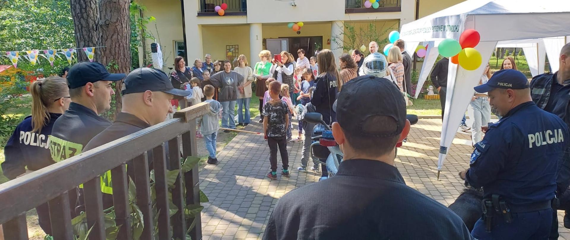 Na zdjęciu strażacy, motocykl policyjny. W tle dom dziecka