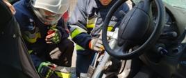 Zdjęcie przedstawia strażaków podczas rozpierania progu samochodu osobowego rozpierakiem kolumnowym