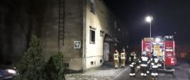 TRAGICZNY POŻAR MIESZKANIA. Na zdjęciu widać budynek mieszkalny w którym doszło do pożaru, pojazd strażacki, wokół niego strażacy