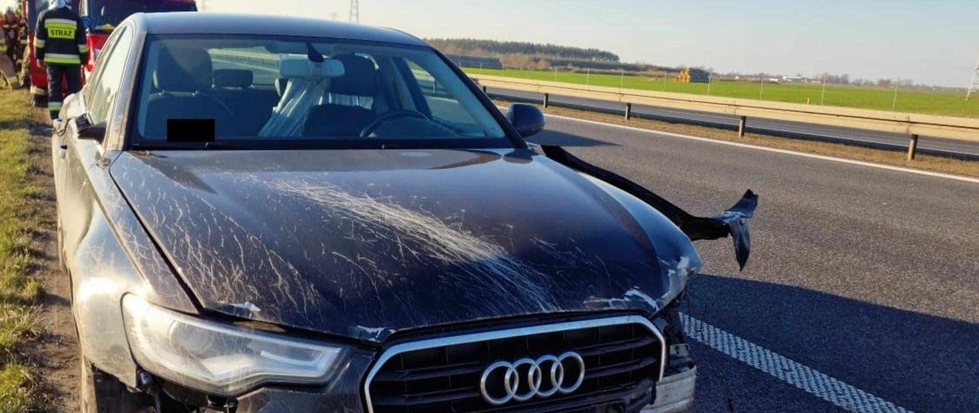 Widać uszkodzony samochód od przodu, pojazd jest na drodze