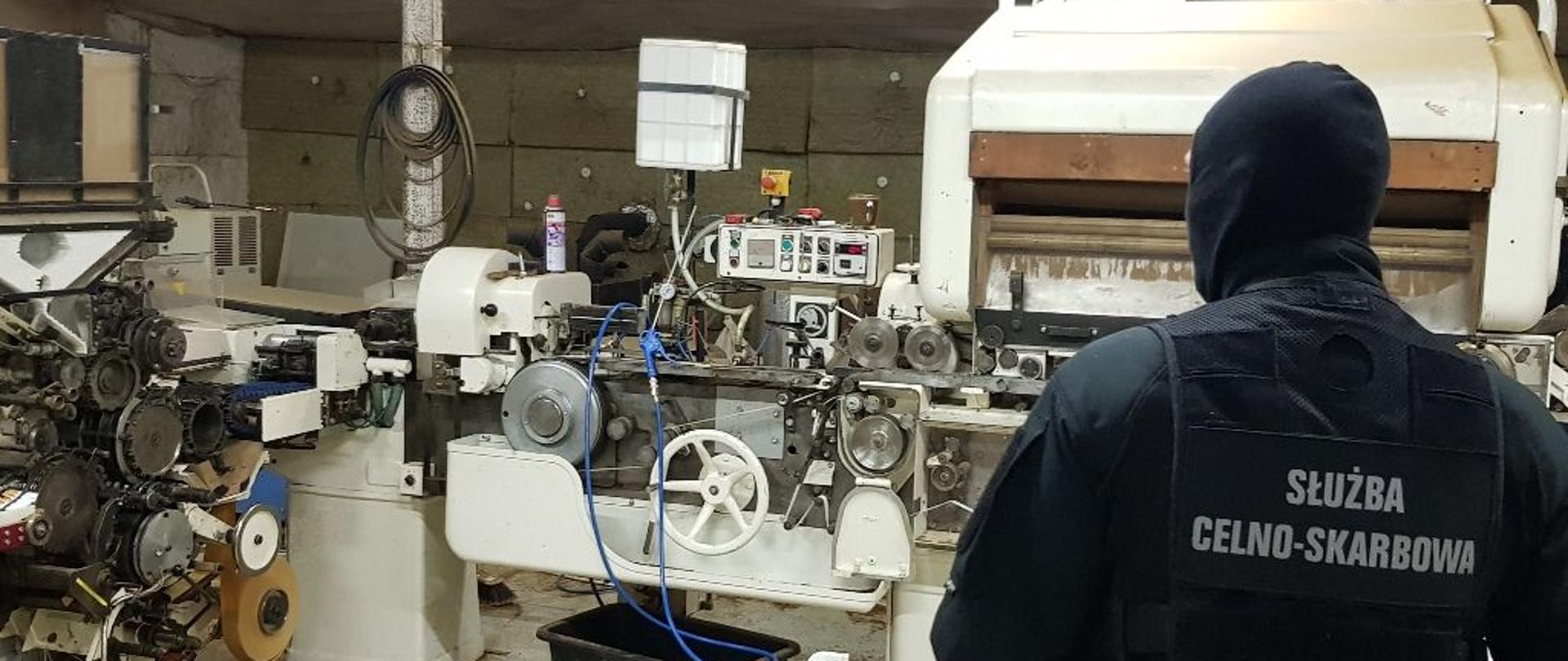 Pomieszczenie z maszyną, z prawej strony funkcjonariusz Służby Celno-Skarbowej.