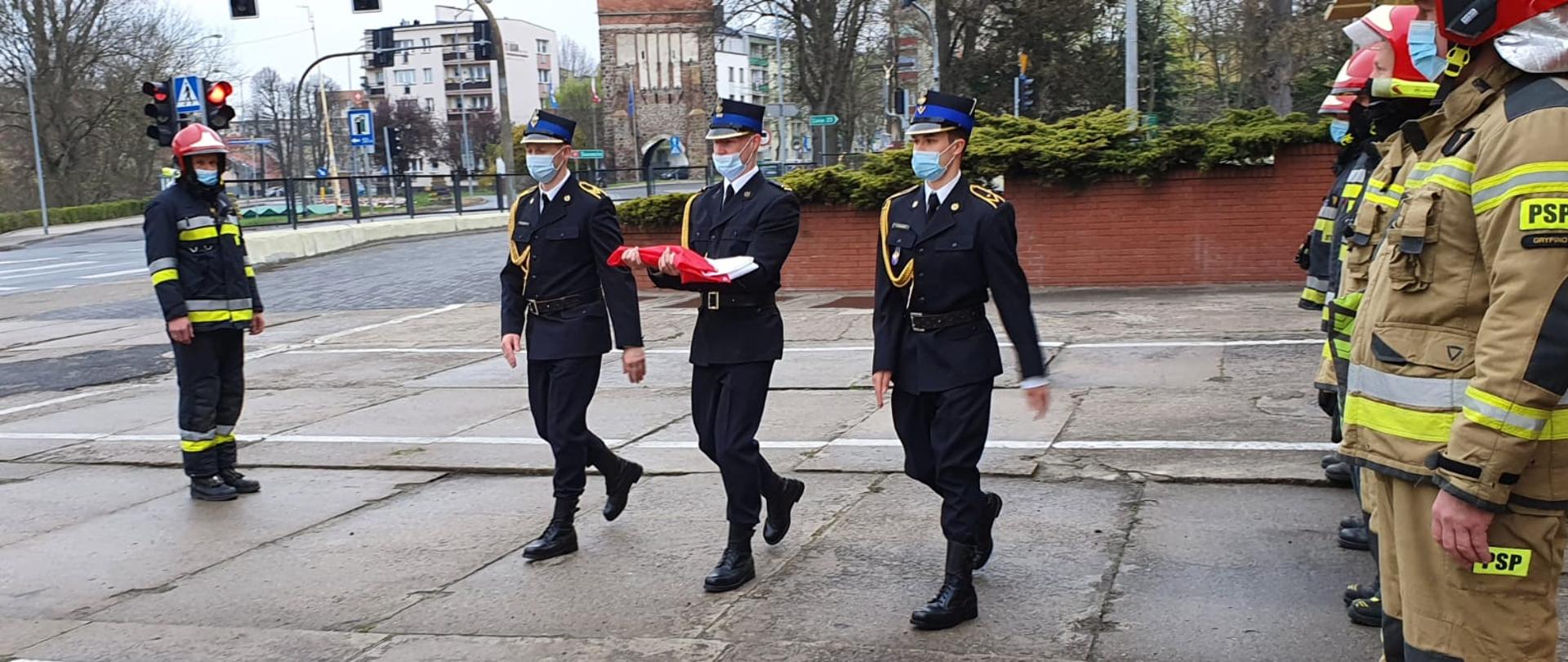 Zdjęcie przedstawia funkcjonariuszy PSP niosących flagę Polski
