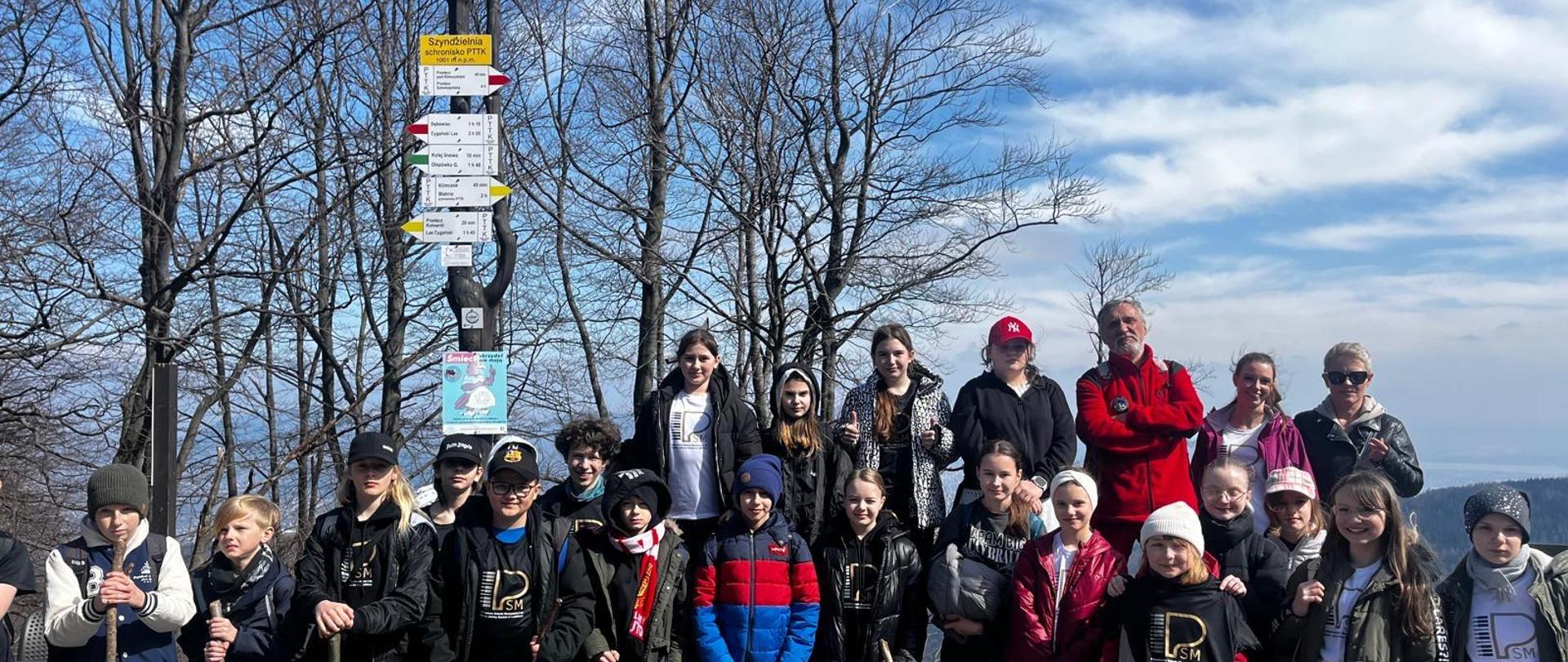 Grupa uczniów i nauczycieli wraz z przewodnikiem na szczycie Szyndzielni w Beskidzie Śląskim podczas wycieczki w dniach 27,28 marca 2025 r. do Bielska-Białej