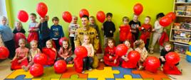 Na zdjęciu widać rozbawioną grupę przedszkolaków z balonami, po środku strażak prowadzący zajęcia.