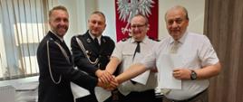 Czterech mężczyzn podaje sobie prawą rękę i pozuje do zdjęcia. Od lewej - dwóch mężczyzn ubranych w mundur strażacki i dwóch ubranych w białą koszulę. 