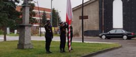 Trzech strażaków przy maszcie montują flagę państwową celem jej podniesienia.