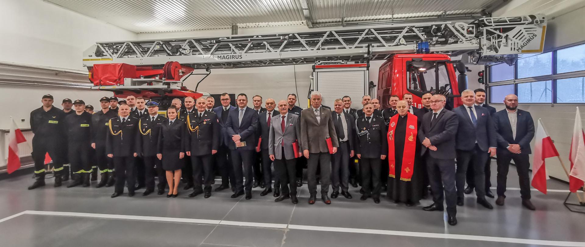 uczestnicy narady - strażacy i zaproszeni goście pozują do zdjęcia na tle nowego samochodu z drabiną mechaniczną