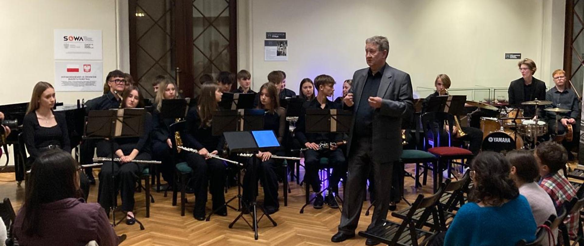 Zdjęcie przedstawia Big Band POSM II stopnia podczas występu w holu Pałacu Radolińskich oraz zgromadzoną publiczność podczas koncertu.