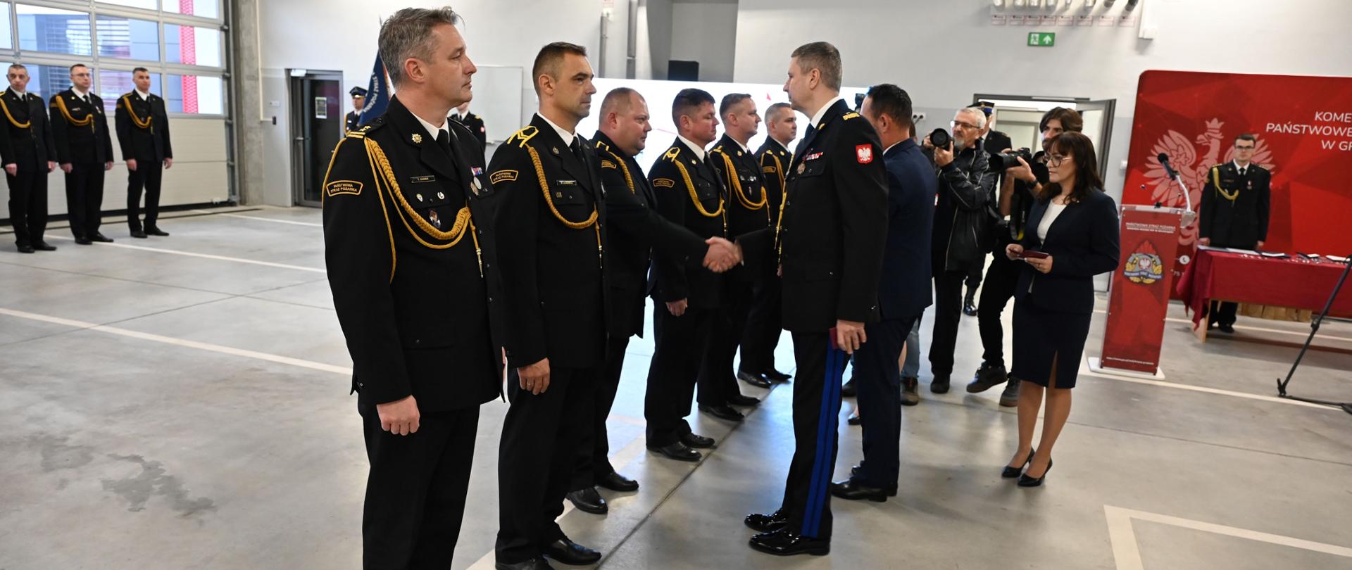 Wręczenie odznaczeń strażakom stojącym w szeregu w hali.