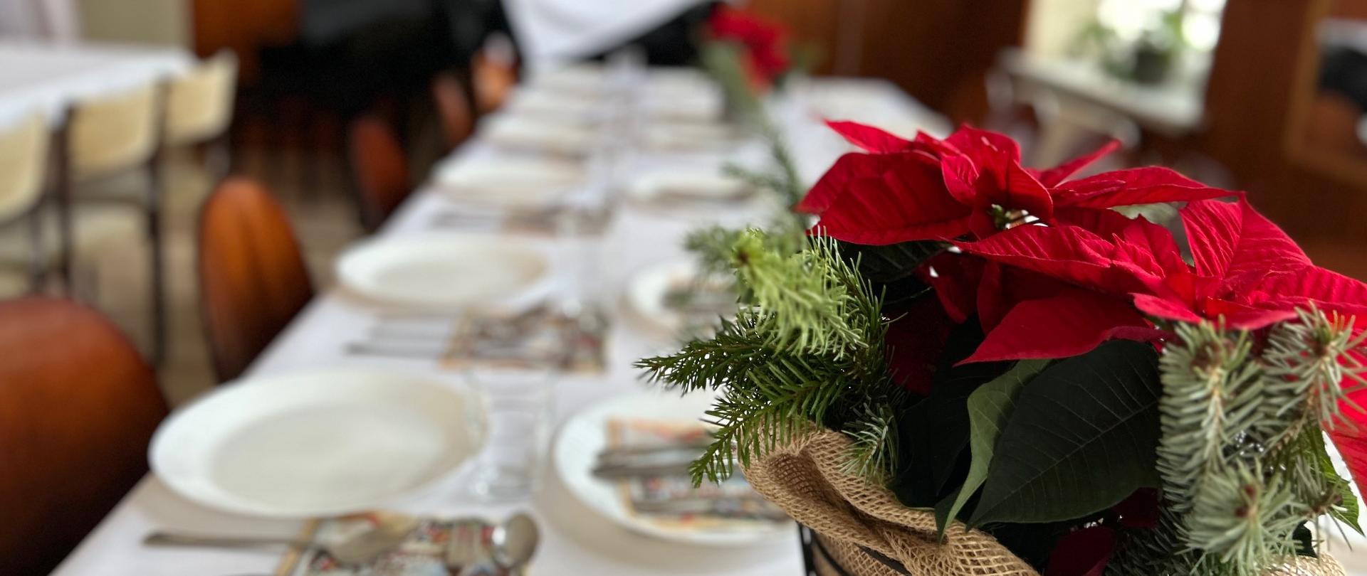 Świątecznie nakryty stół z talerzami i sztućcami, udekorowany czerwonym gwiazdorem i gałązkami świerku, przygotowany na kolację wigilijną w sali szkoły.